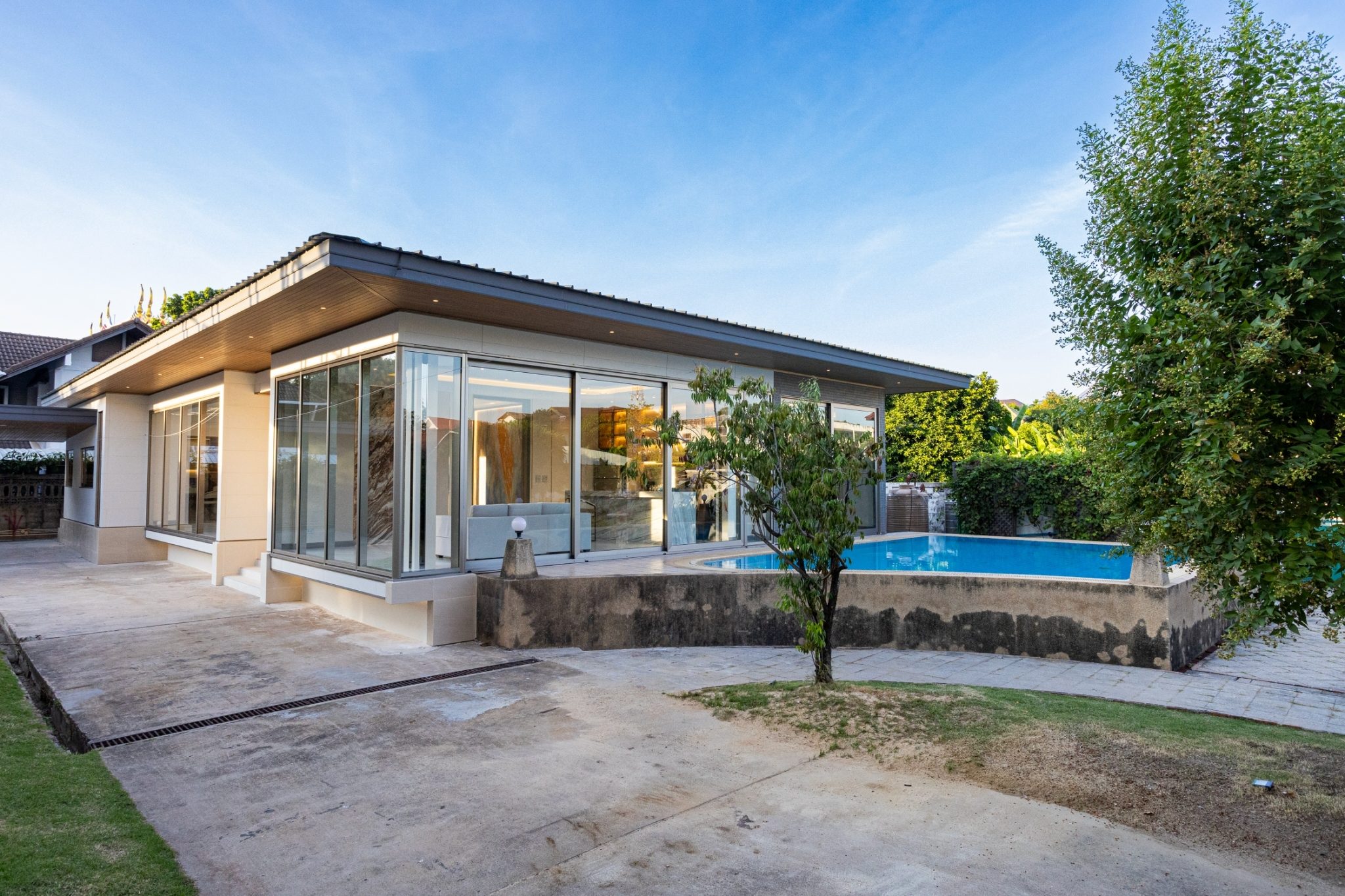 A single-storey house in Dusit, Bangkok, with an Aluk SL50 glass corner in slim grey frames beside the pool