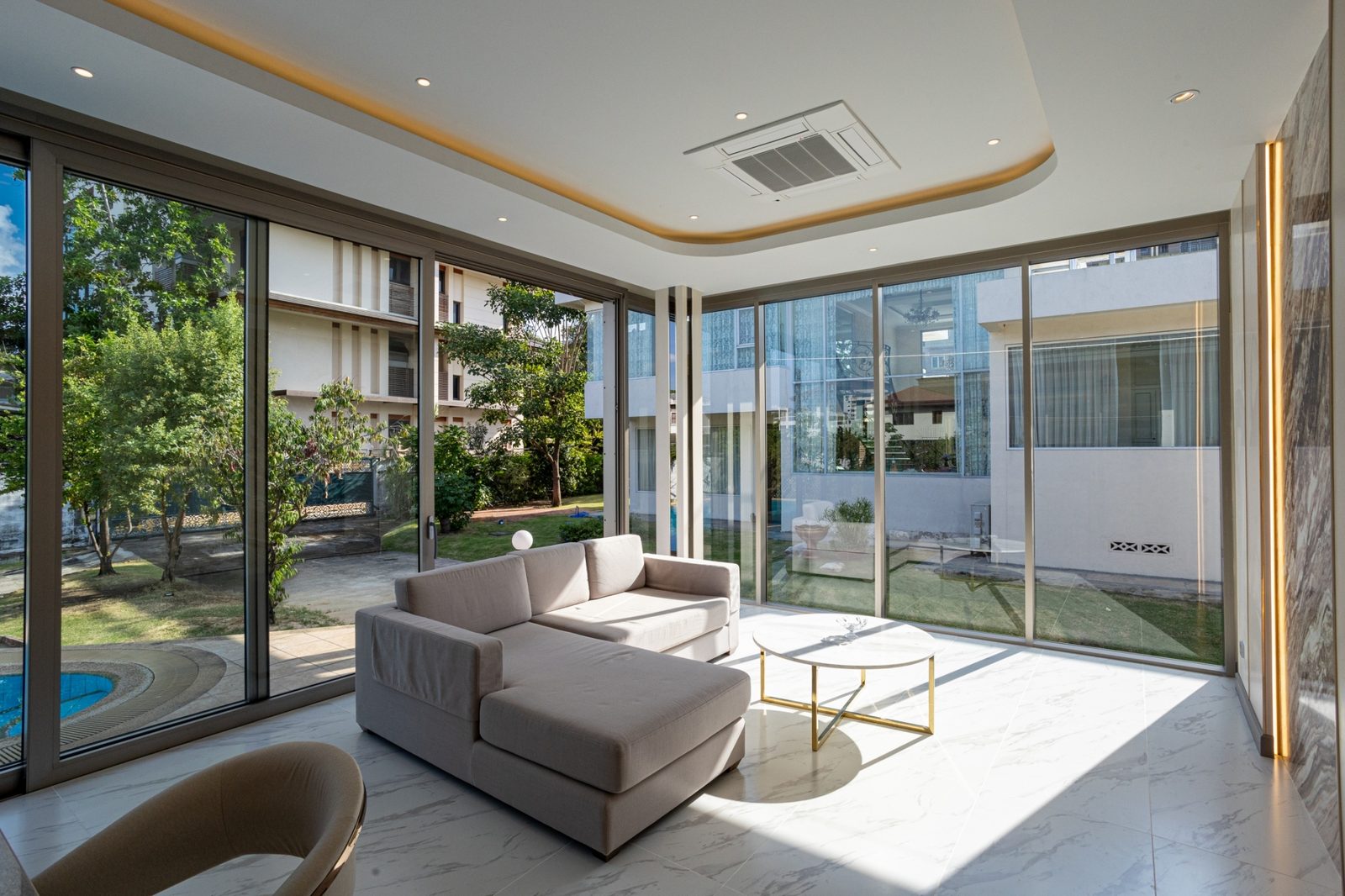 A sunlit living room with a corner of floor-to-ceiling glass in slim Aluk SL50 frames, looking out to the pool and garden