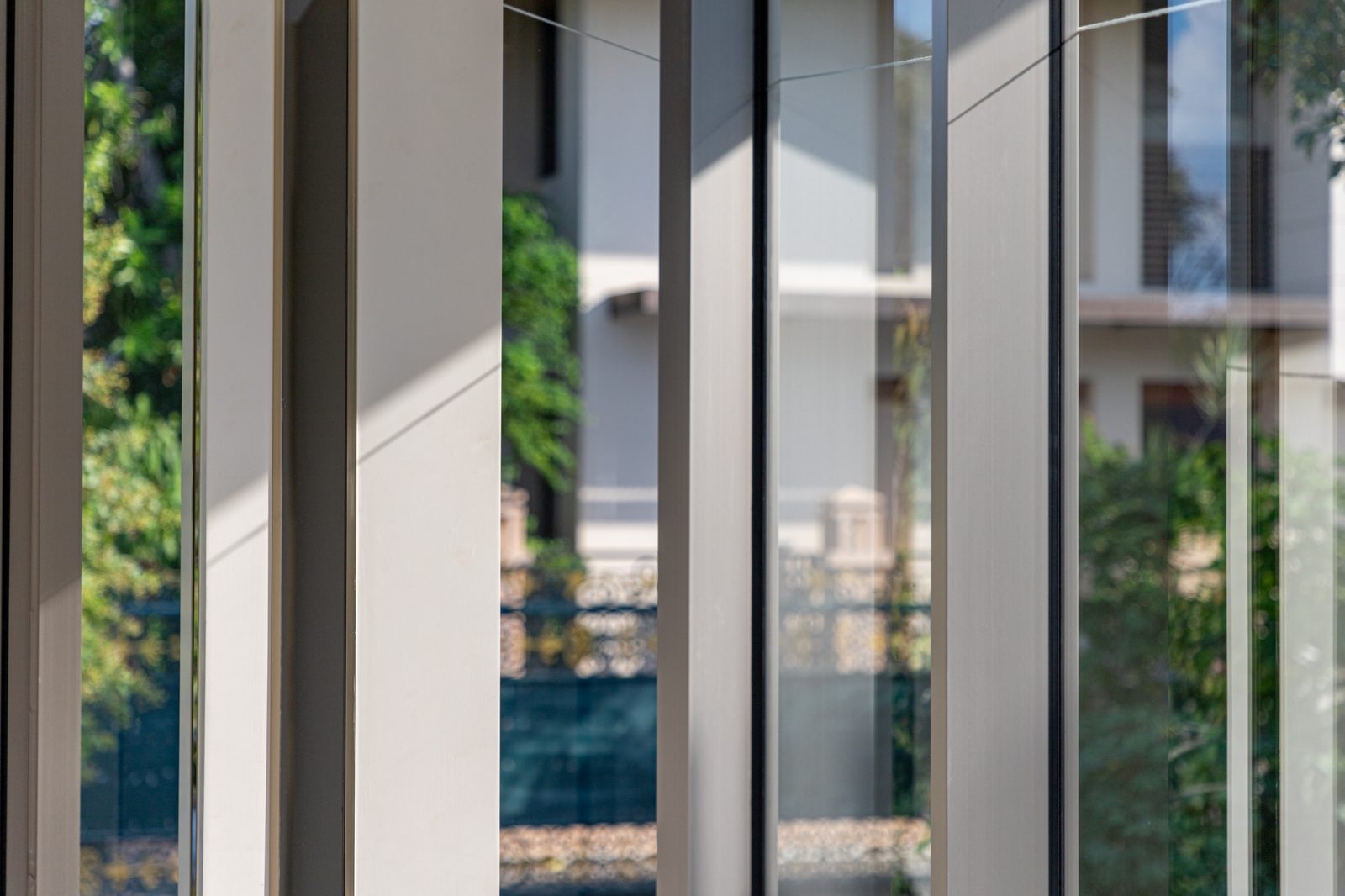 Close-up of slim champagne-grey Aluk SL50 mullions in sunlight, the garden soft behind the glass