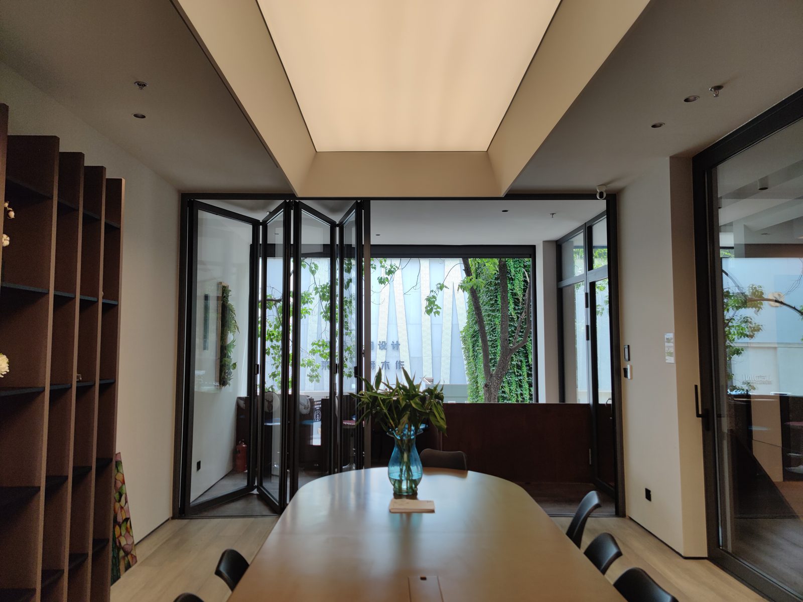 Dark-framed VBM FD-95 bi-folding panels folding open behind a meeting table, trees outside