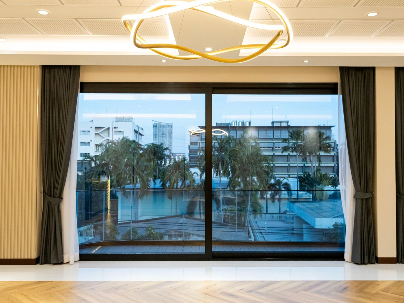 A two-panel sliding glass door in black frames, in a room with a herringbone floor and charcoal curtains, looking out to the balcony and the city