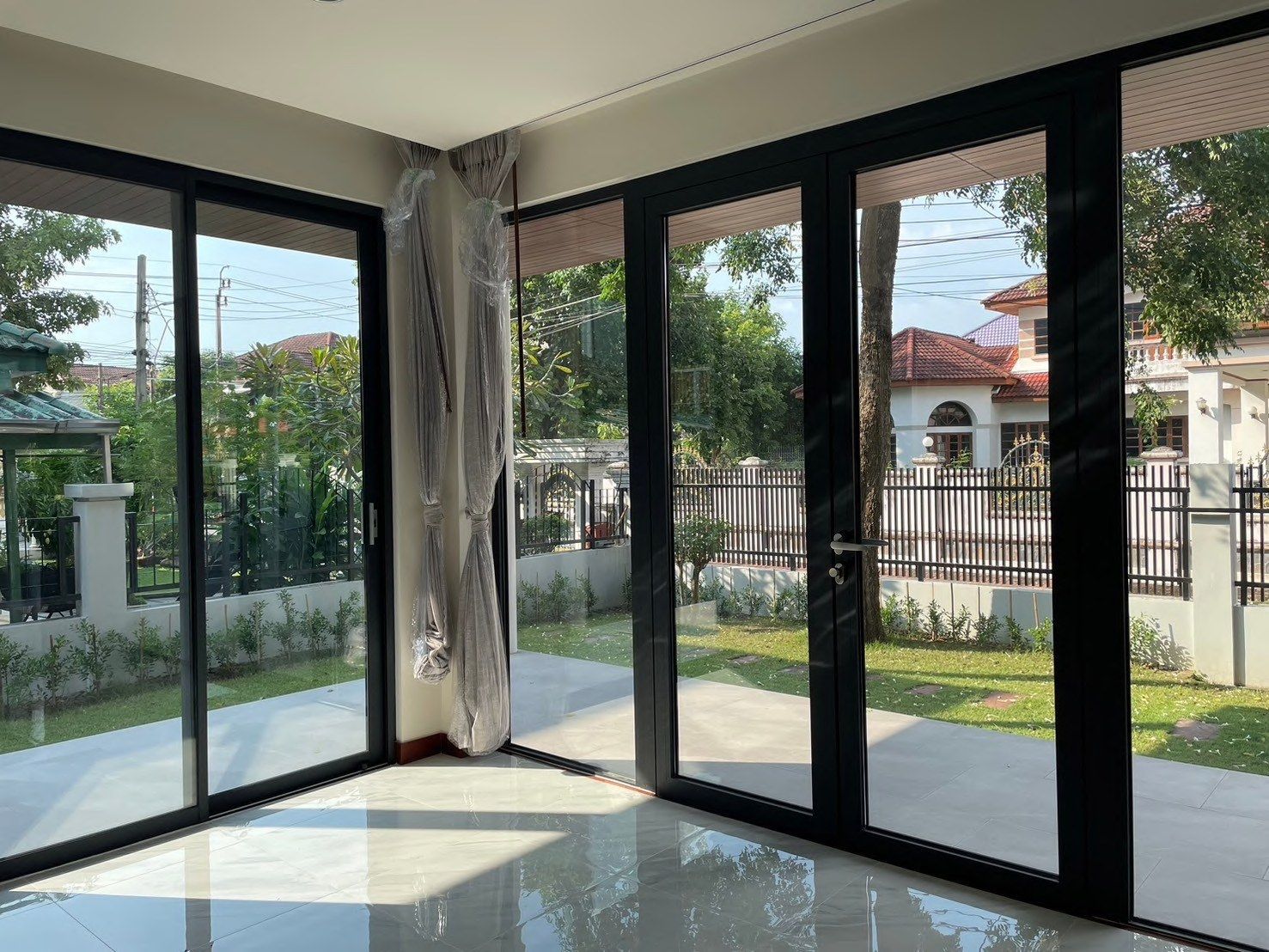 A hall with a polished floor and black-framed aluminium glass doors opening onto the front garden