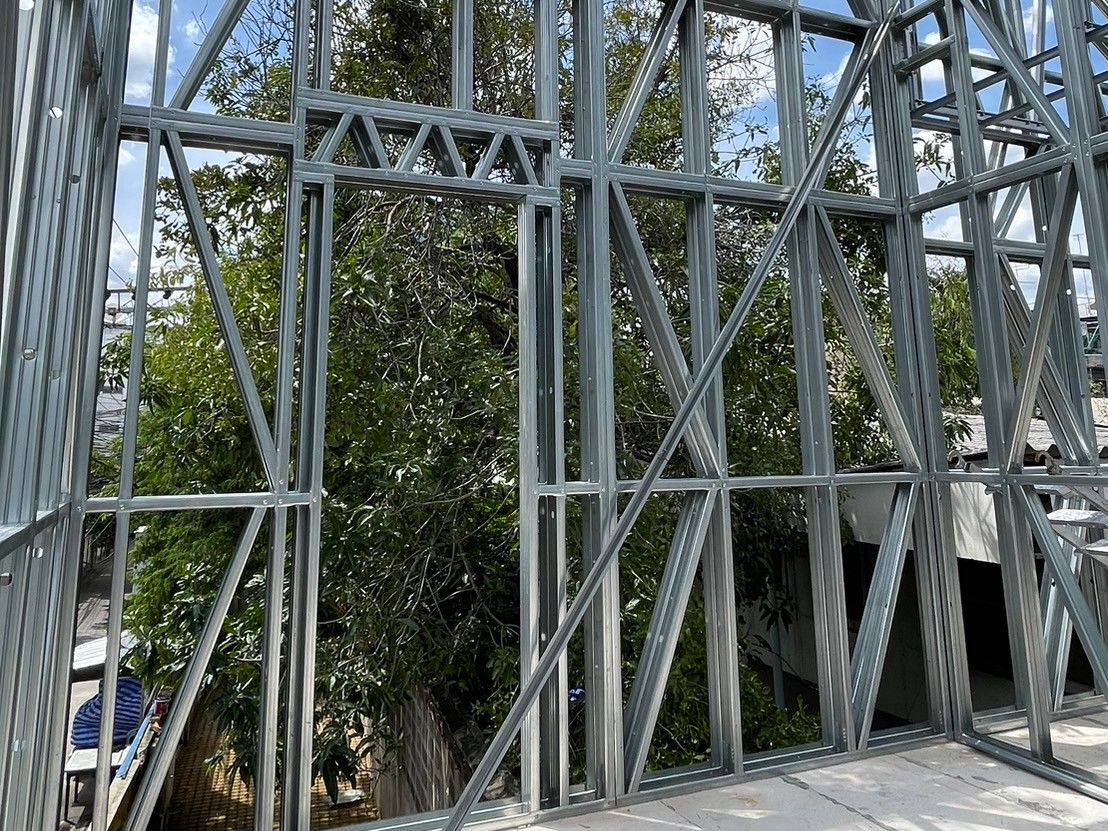 A light gauge steel wall with a floor-to-lintel opening, a small steel truss spanning it as the lintel and diagonal bracing on both sides, trees beyond