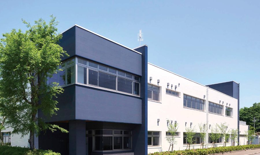 A two-storey office and research building in Japan re-clad in navy and white flat panels, with a band of windows on the corner block