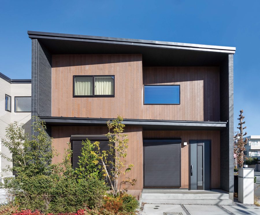 A two-storey house in Japan clad in vertical brown wood-look boards under a deep flat roof, framed by dark side walls