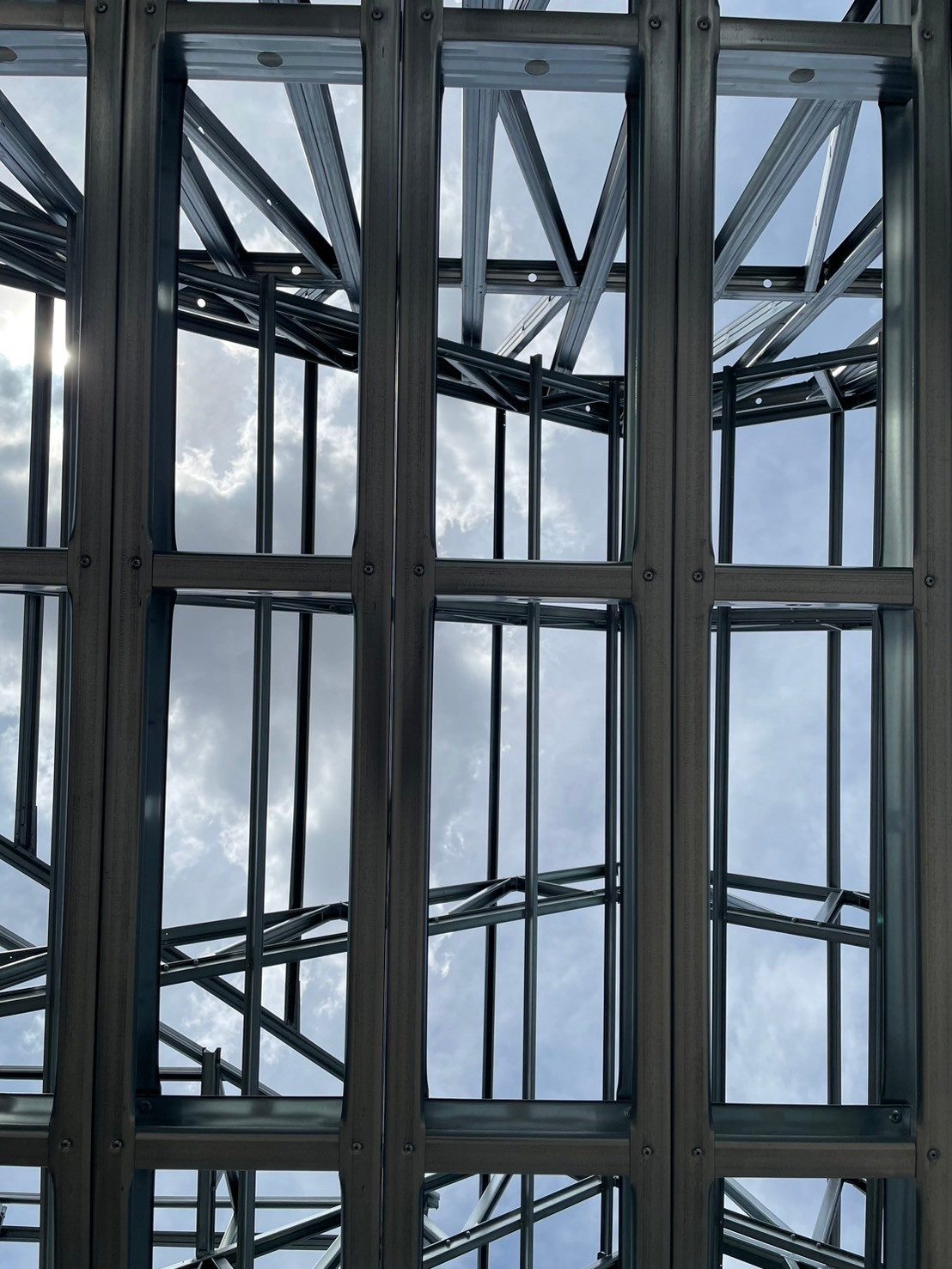 Coated steel wall studs, noggings and a top track with roof trusses above, seen from below against the sky