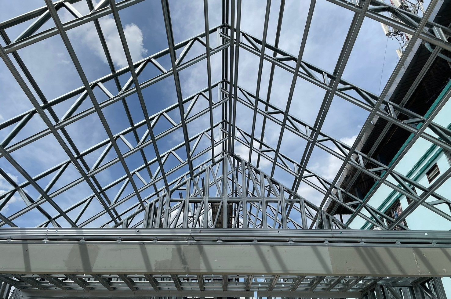 Coated steel roof trusses rising to the ridge above a steel gable wall, seen from inside against a blue sky
