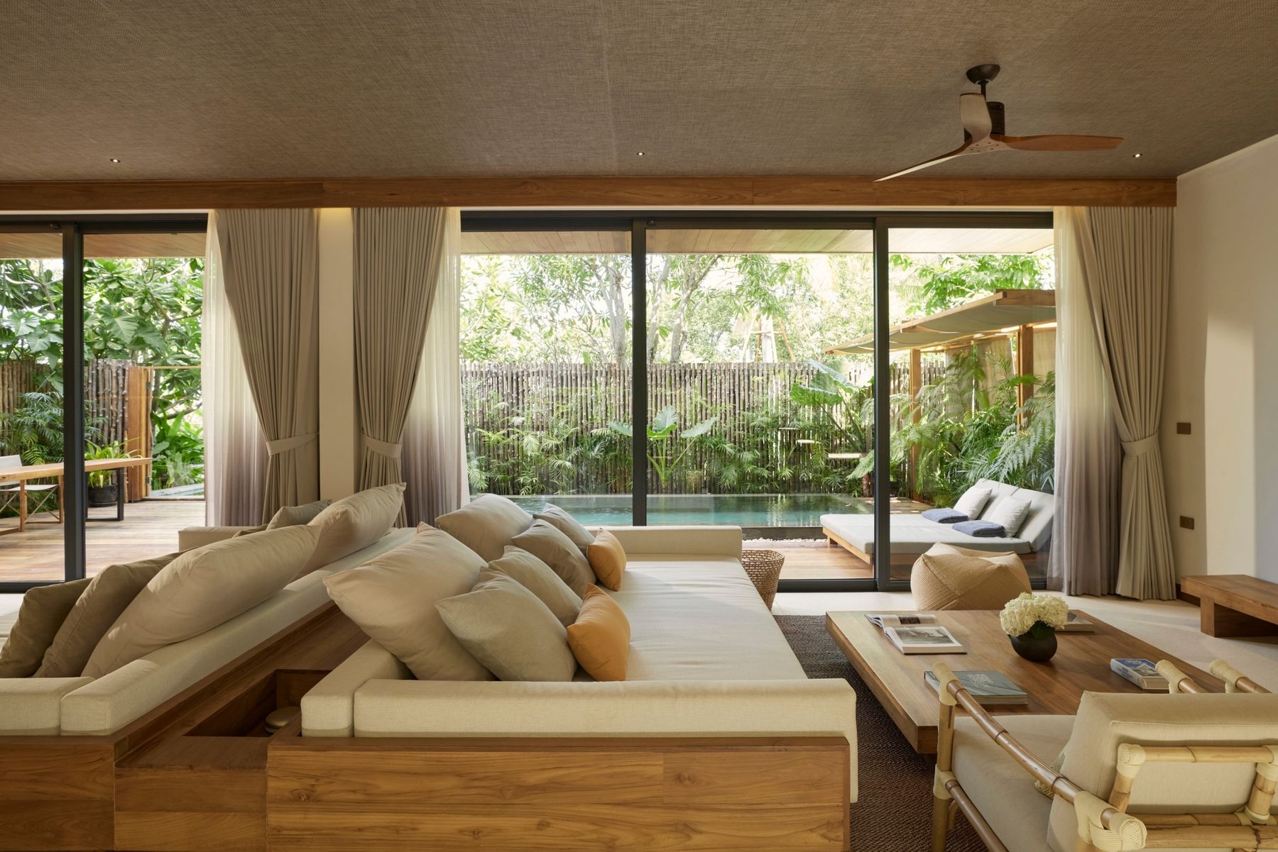 A pool villa living room, its sofa facing the pool and garden through wide glass doors