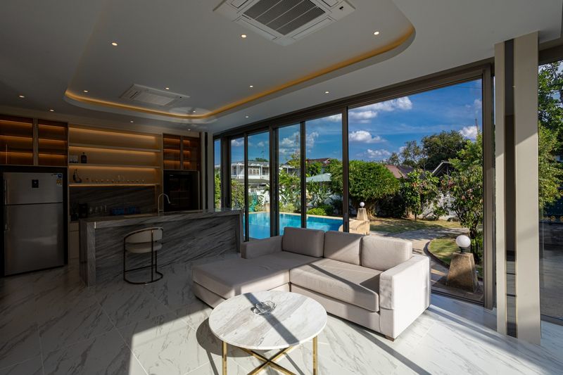 A finished living room and kitchen with floor-to-ceiling glass onto the pool and garden