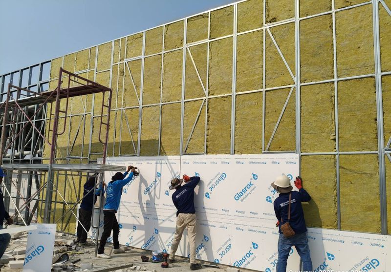 Installers fixing boards over insulation on a building's steel frame