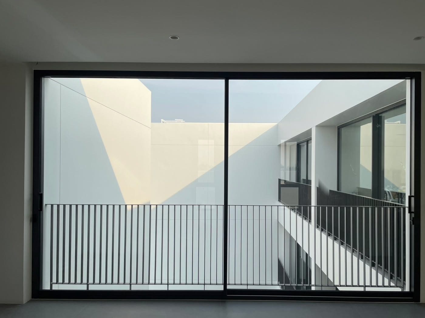 A two-panel Technal LUMEAL sliding door in black frames looks onto a sunlit white courtyard, one slim interlock down the middle