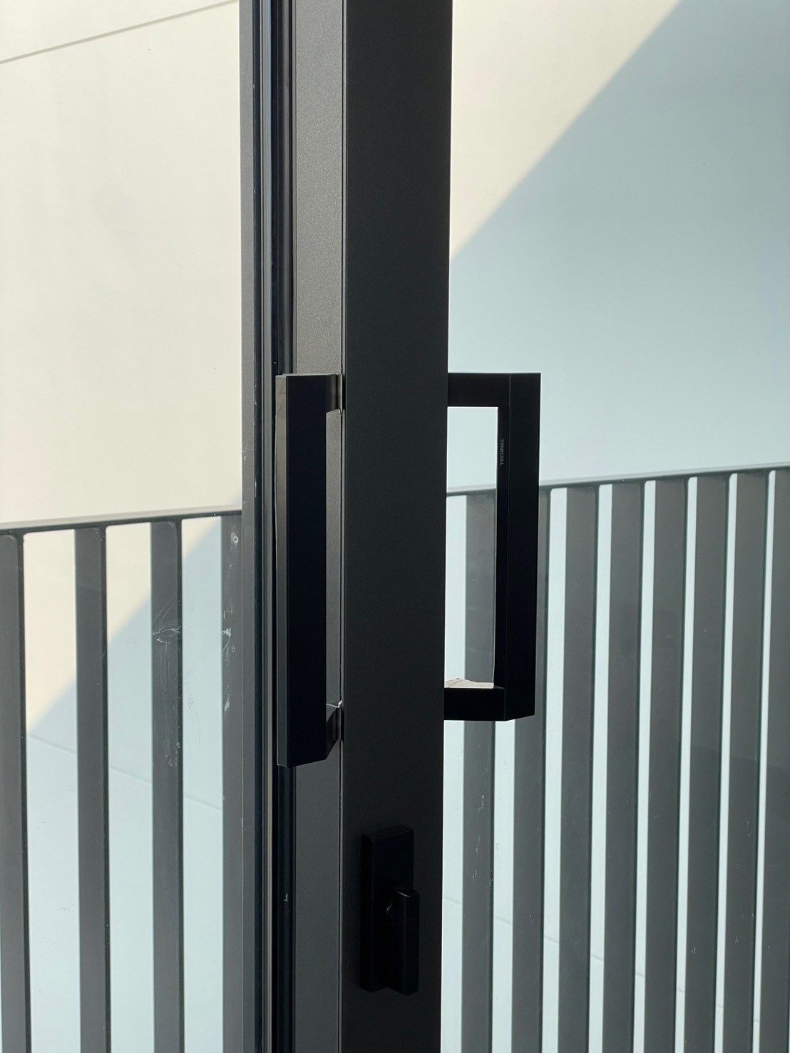 Matt black square pull handles on a Technal LUMEAL sliding door where the two panels meet, with a black lock below