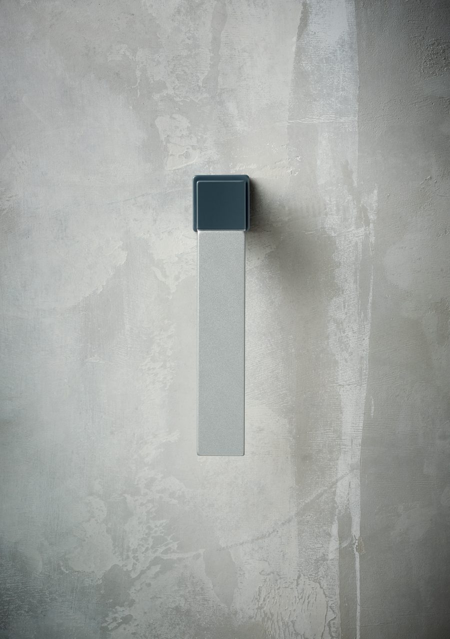 A Technal TEMPTATION window handle combining a dark blue-grey top with a light grey lever, on a pale plaster wall