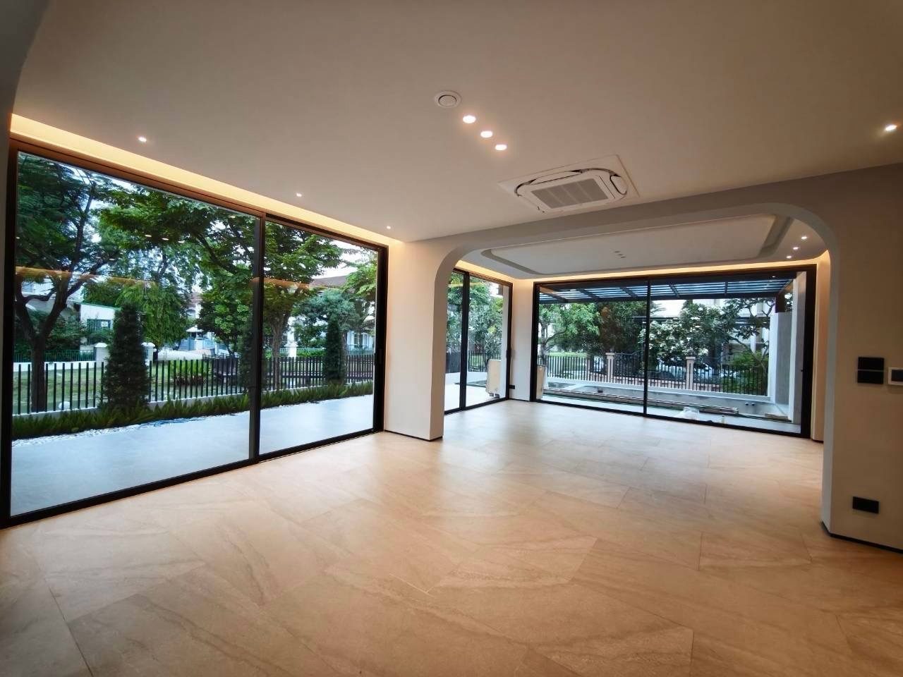A living room with floor-to-ceiling sliding glass doors on two walls, an arched opening and warm cove lighting